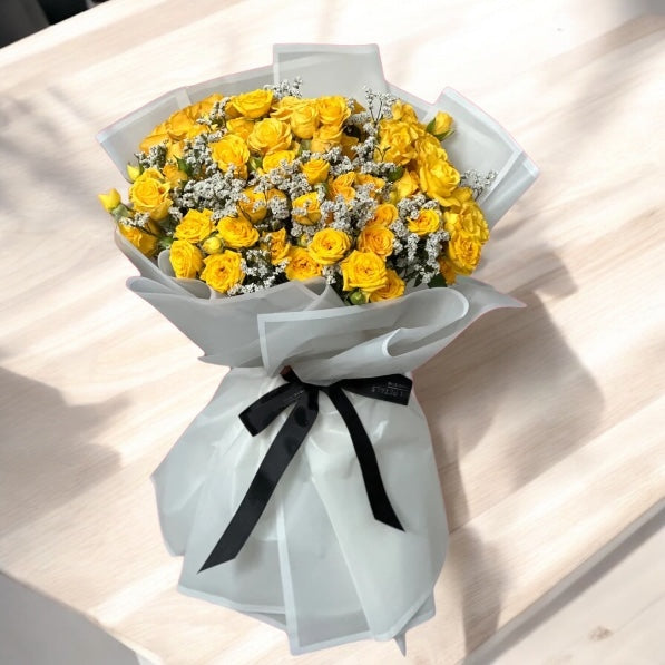 A bouquet of yellow roses with green leaves, arranged and tied with a ribbon.